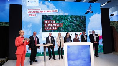 Sieben Personen stehen auf einer Bühne in einer Reihe, im Hintergrund ein großer Bildschirm zur Preisverleihung des Wettbewerbs "Gemeinsam stark sein 2022"